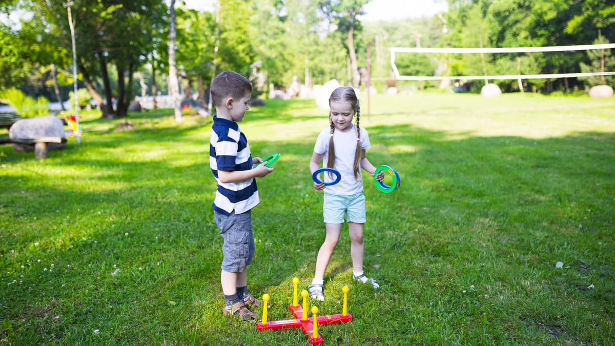 Two kids enjoying a ring toss game outdoors in a sunny park setting.